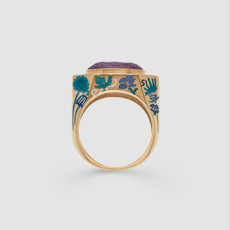 Gold ring with floral design and purple stone on a light gray background