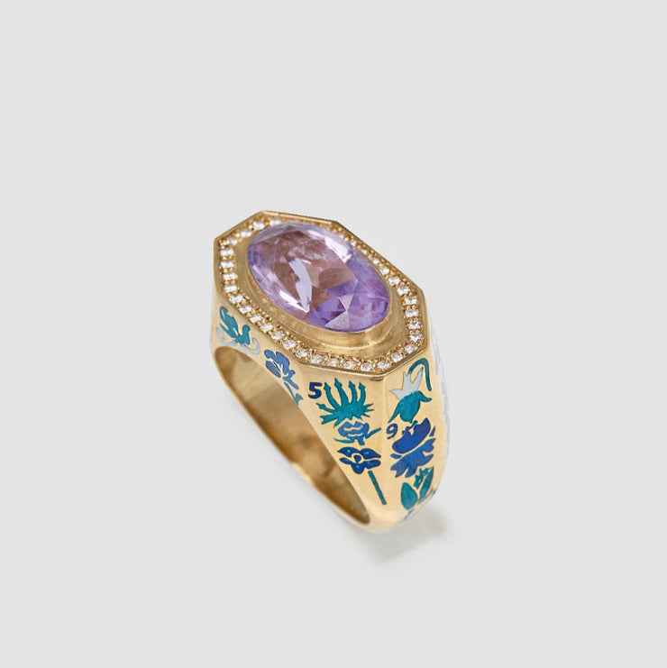 Gold ring with a purple gemstone and blue floral design on a light gray background